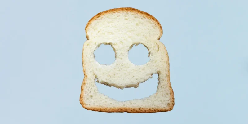 a piece of bread with two eyes and a happy face punched out on a light blue background