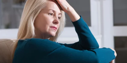 Sad depressed woman at home sitting on the couch, looking down and touching her forehead, loneliness and pain concept