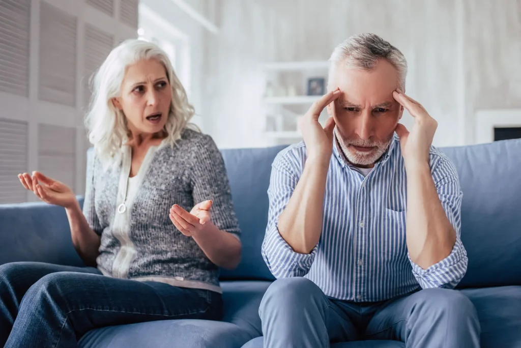 nagging wife sitting on the couch complaining at her husband next to her with his hands on his head