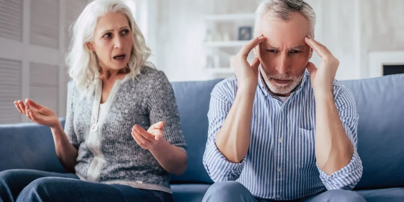nagging wife sitting on the couch complaining at her husband next to her with his hands on his head