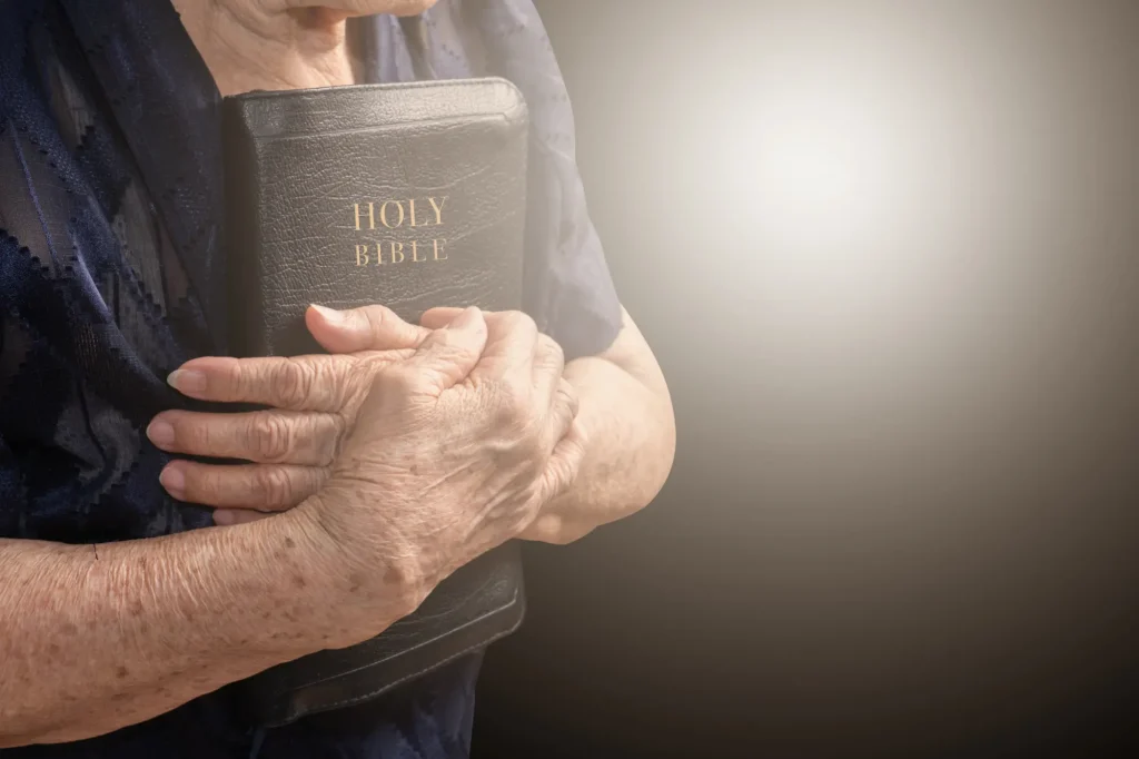 Older adult holding a bible in preparation for prayer.