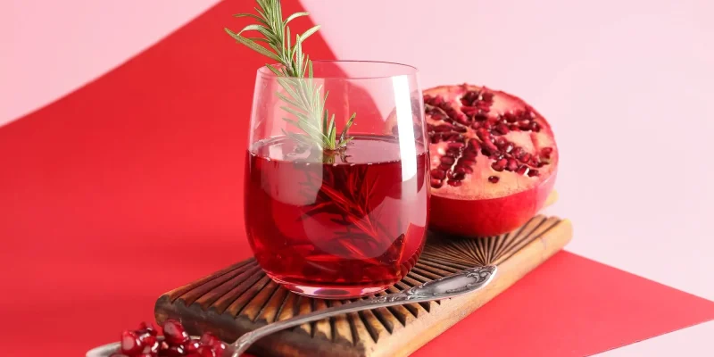 Board with glass of fresh pomegranate juice on colorful background
