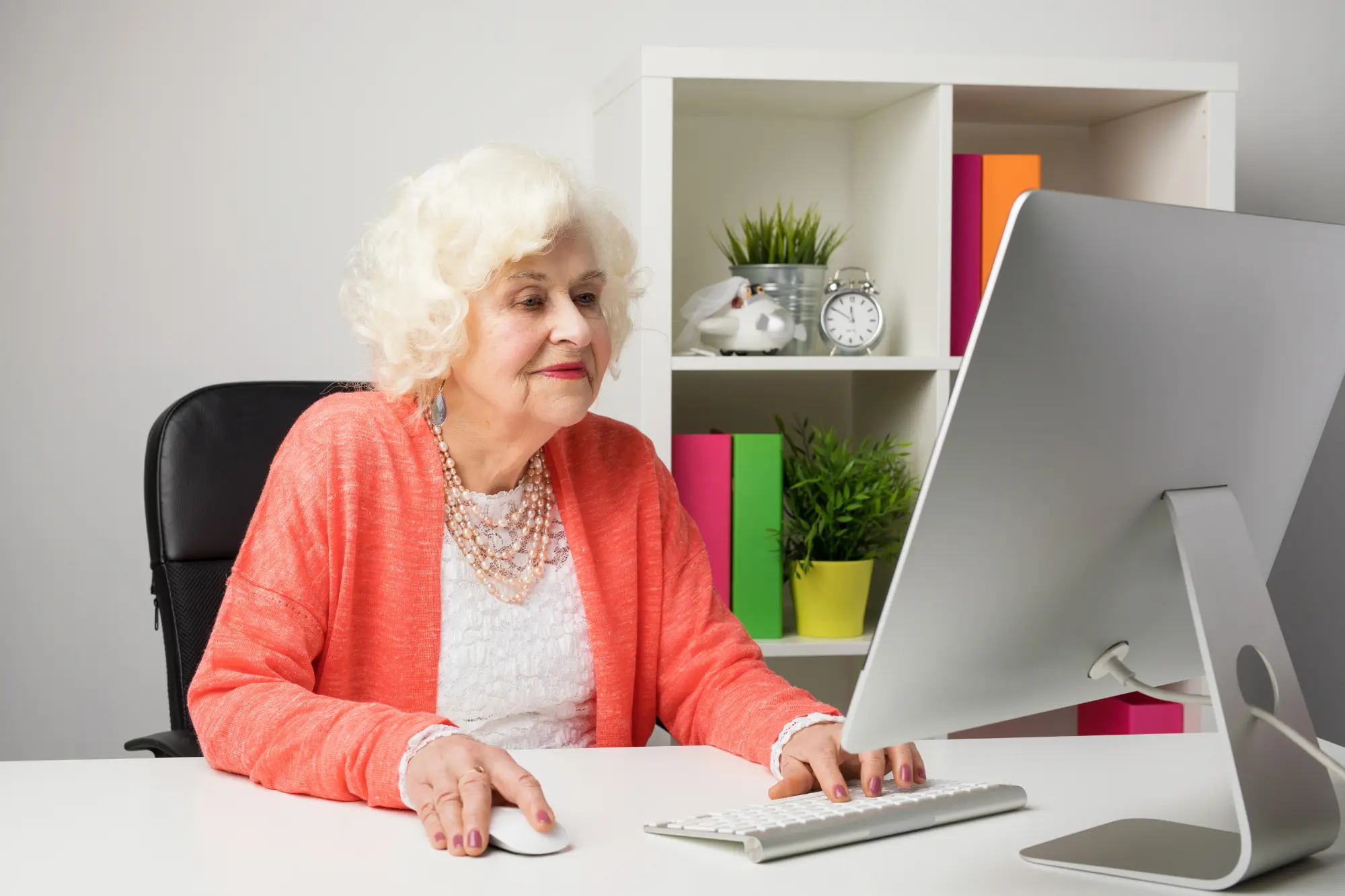 elderly senior woman wearing a pink color sweater looking at a computer screen