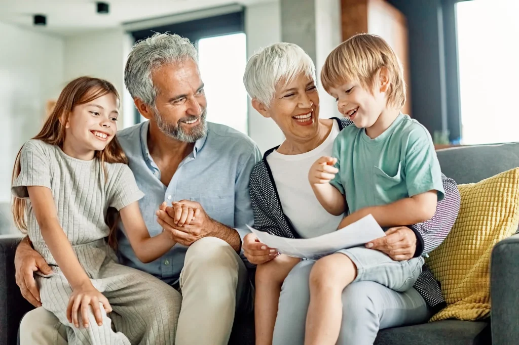 supportive grandparents sitting with smiling grandchildren looking at papers, maybe homework