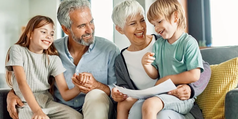 supportive grandparents sitting with smiling grandchildren looking at papers, maybe homework