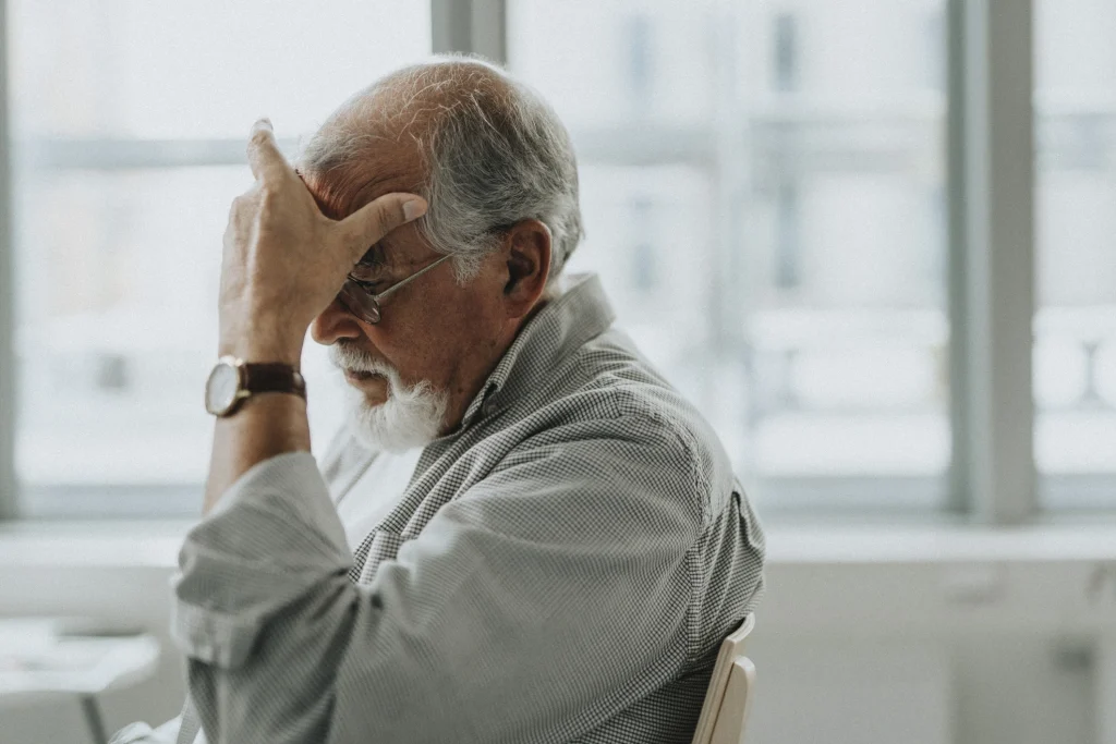 senior adult man sitting in chair with hand over face looking like he just recieved bad or life changing news