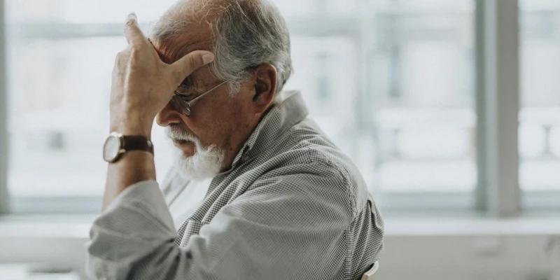 senior adult man sitting in chair with hand over face looking like he just recieved bad or life changing news