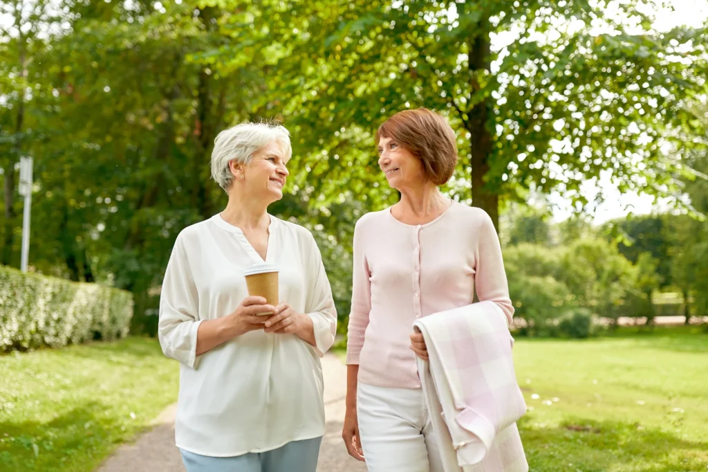 two senior women walking outside and drinking coffee and talking