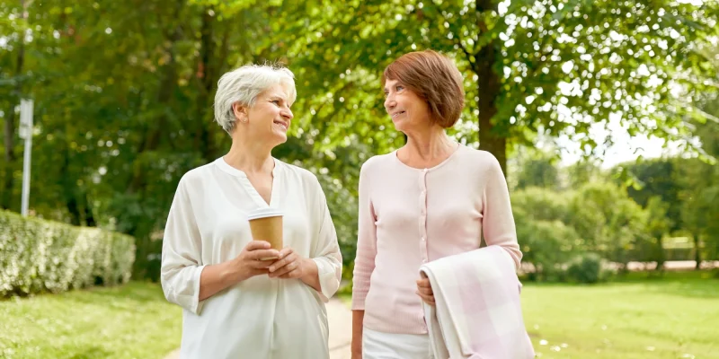 two senior women walking outside and drinking coffee and talking