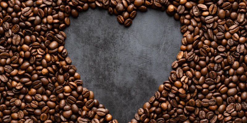 Heart made of coffee beans on black concrete background. Black and brown heart. Love coffee concept. top view