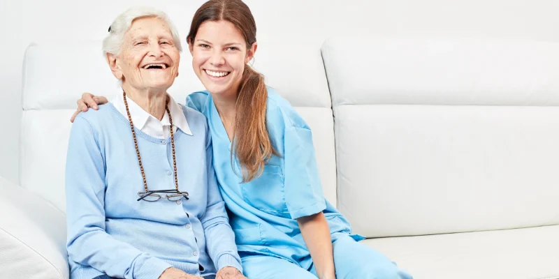 nurse and senior woman on couch smiliing