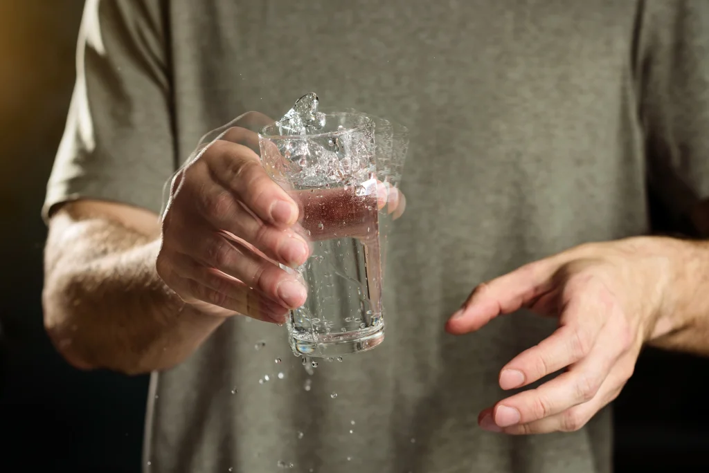 A man holds a glass of water with a shaking hand. The concept of parkinson's disease and tremor