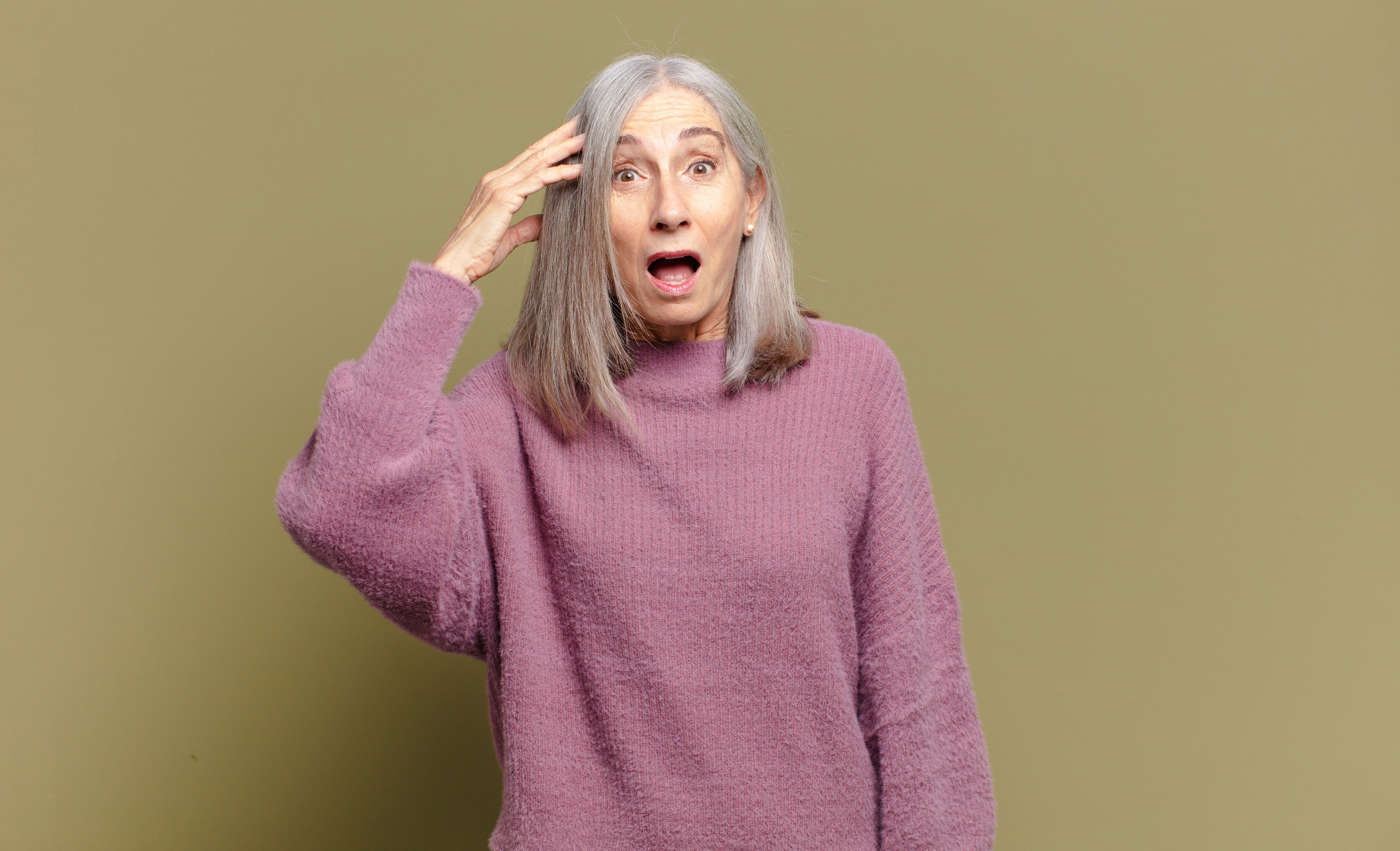 senior woman wearing a purple sweater looking surprised by good news
