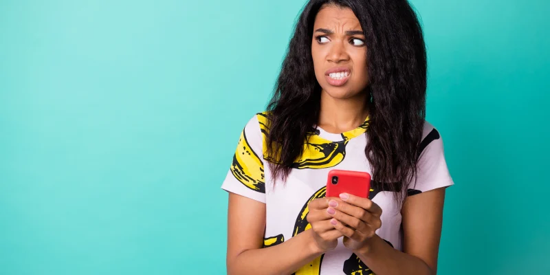 Photo of disgusted displeased girl hold phone look empty space wear banana print t-shirt isolated turquoise color background