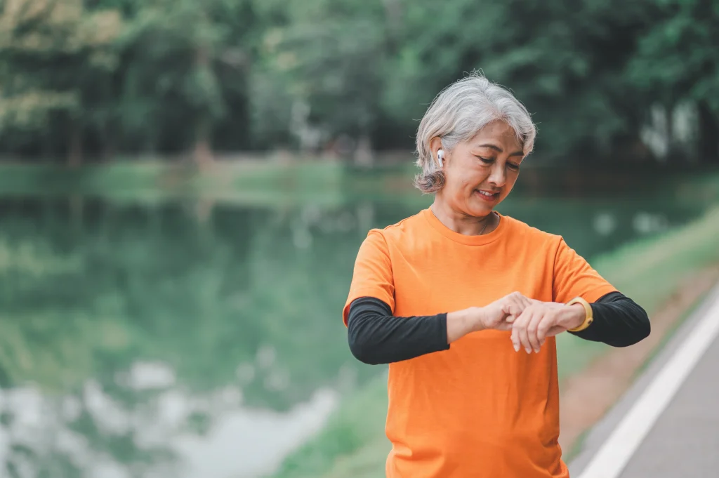Elderly, white-haired Asian woman exercising in the park early in the morning end of run, recovering