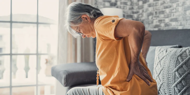 senior woman sitting on couch with osteoporosis back pain