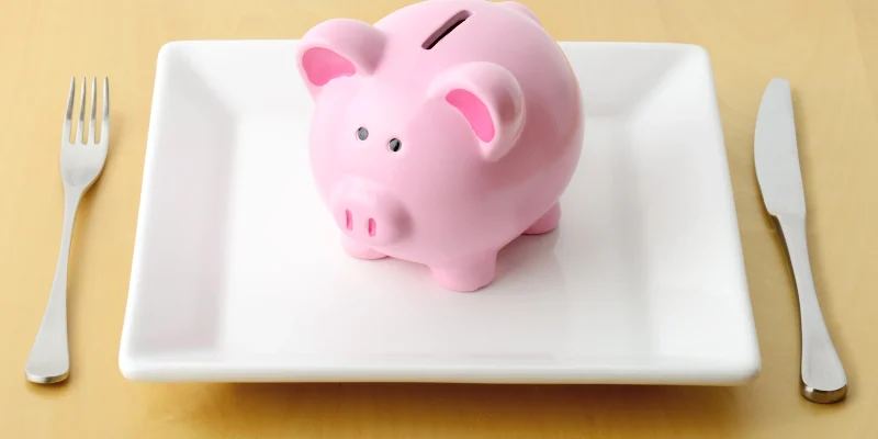 Piggy bank on the plate with fork and knife