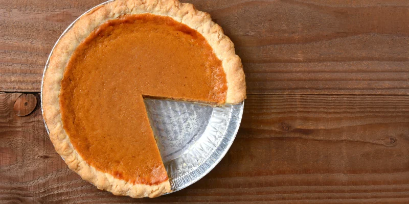 A pumpkin pie with a slice cut out. Horizontal format on a rustic wood table.