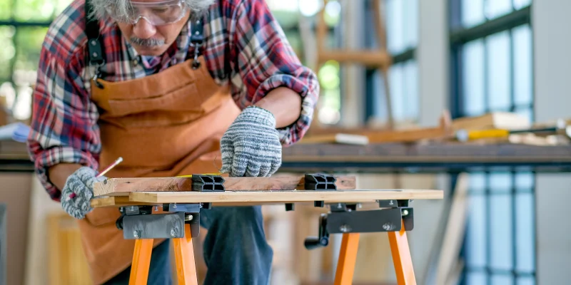 Old or senior Asian craftsman or carpenter act as measurement of wood in the room with wood pile and surround with glasses. Concept of activity for senior generation support good health