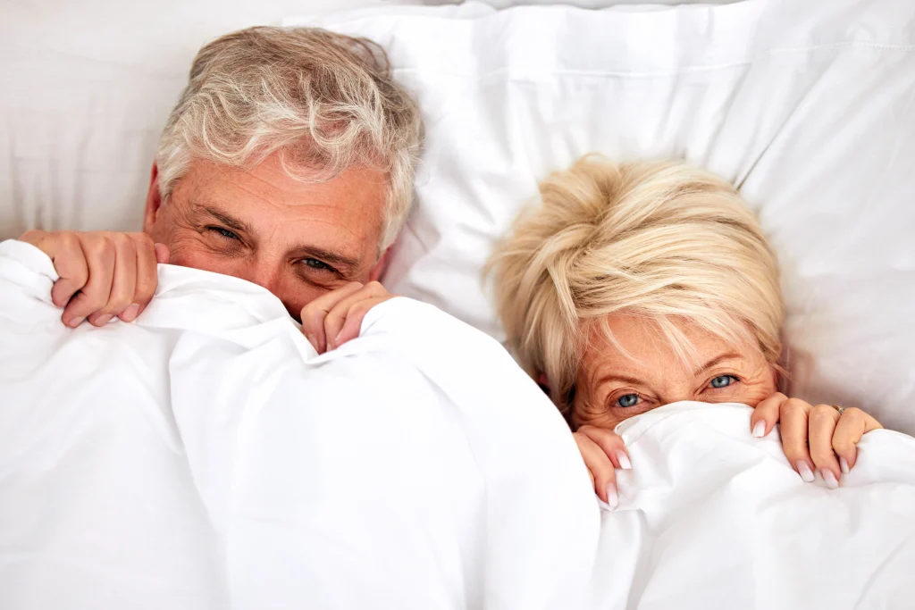 senior couple in bed smiling with covers over faces