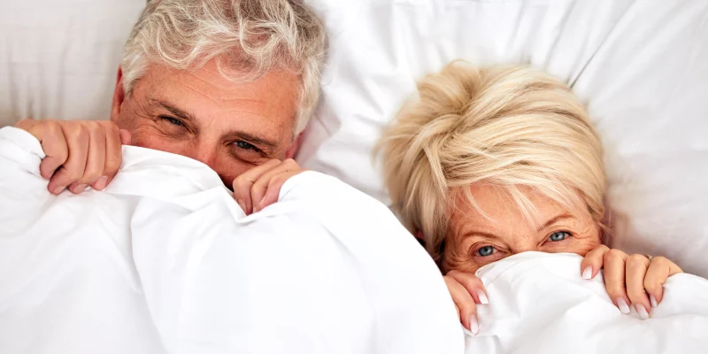 senior couple in bed smiling with covers over faces