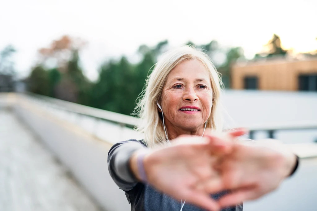 A senior woman with earphones outdoors doing exercise