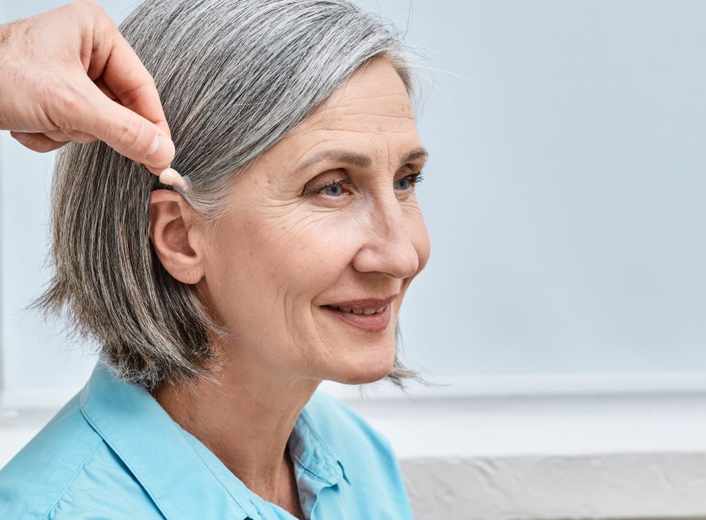 Audien Atom 2 on a senior woman Installation hearing aid on senior woman's ear at audiology center, close-up, side view. Deafness treatment, hearing solutions