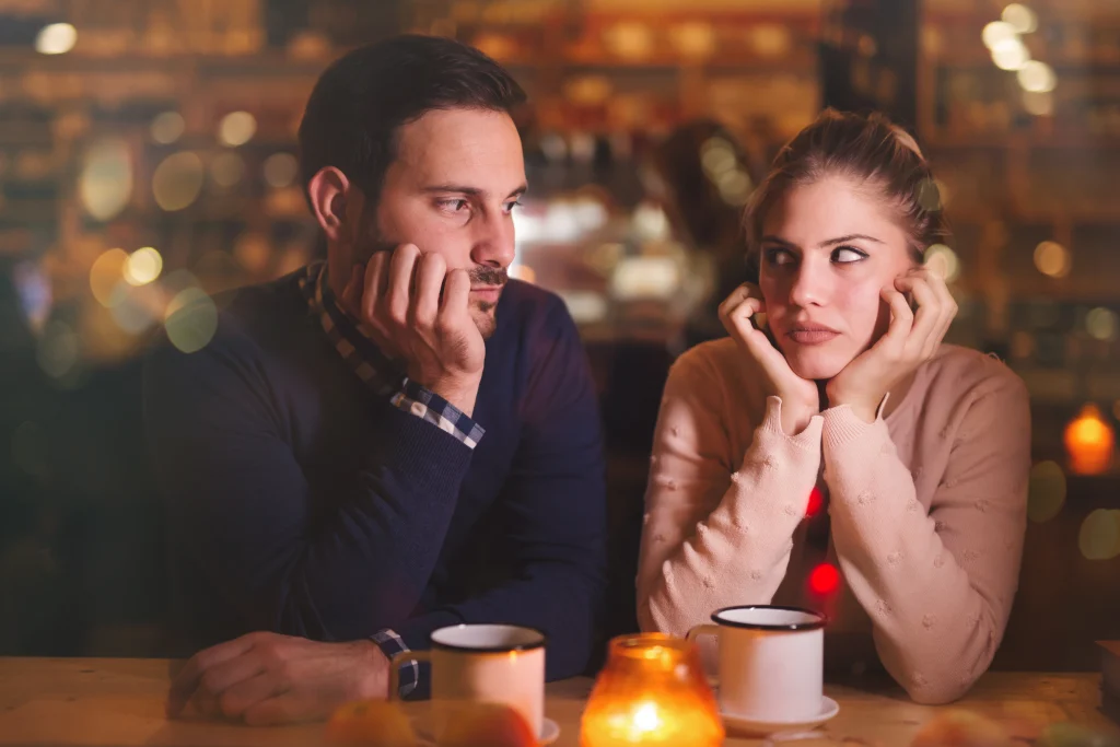 annoyed couple sitting looking bored at a restaurant or meal with family on a holiday like thanksgiving or christmas