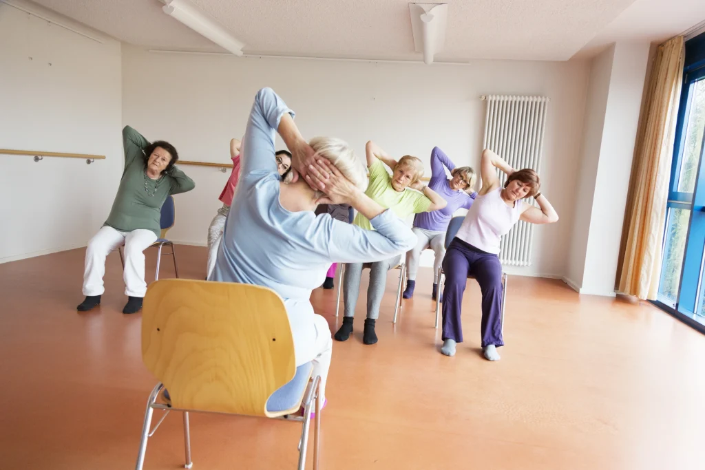 senior women exercising yoga and pilates sitting on chairs, following the instruction of their teacer