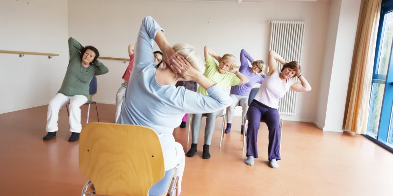 senior women exercising yoga and pilates sitting on chairs, following the instruction of their teacer