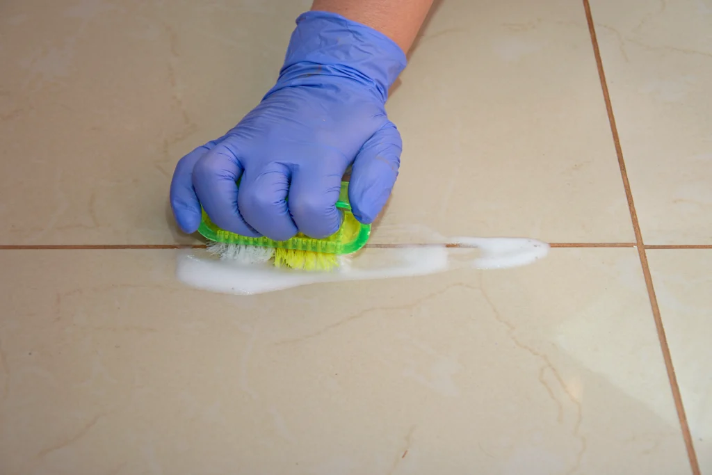 Cleaning the grout in tiles with a brush and detergent. Hands protected by gloves. Strong washing agents. Scrub the dirty joint with foam.