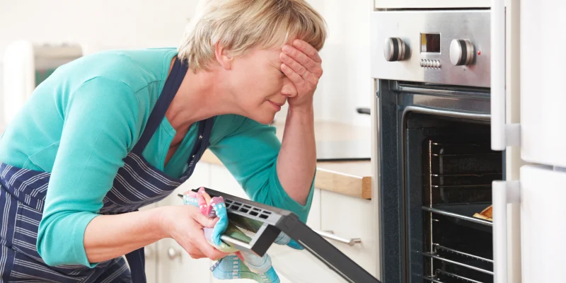 Woman Looking In Oven And Covering Eyes Over Disastrous Meal