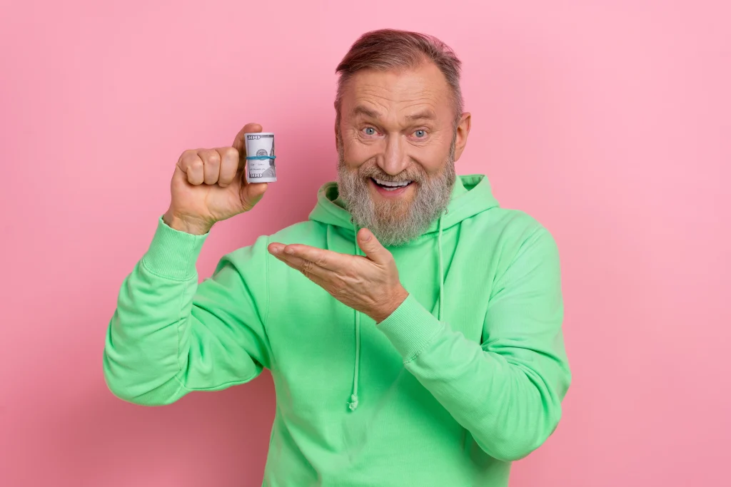 Photo of good mood excited man wear green sweatshirt showing arm dollars roll isolated pink color background