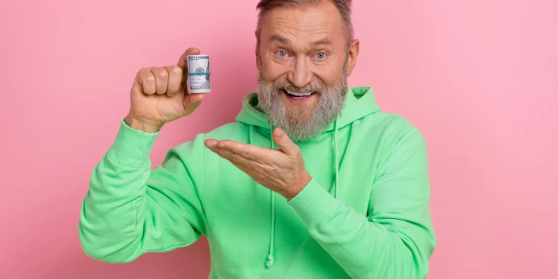 Photo of good mood excited man wear green sweatshirt showing arm dollars roll isolated pink color background