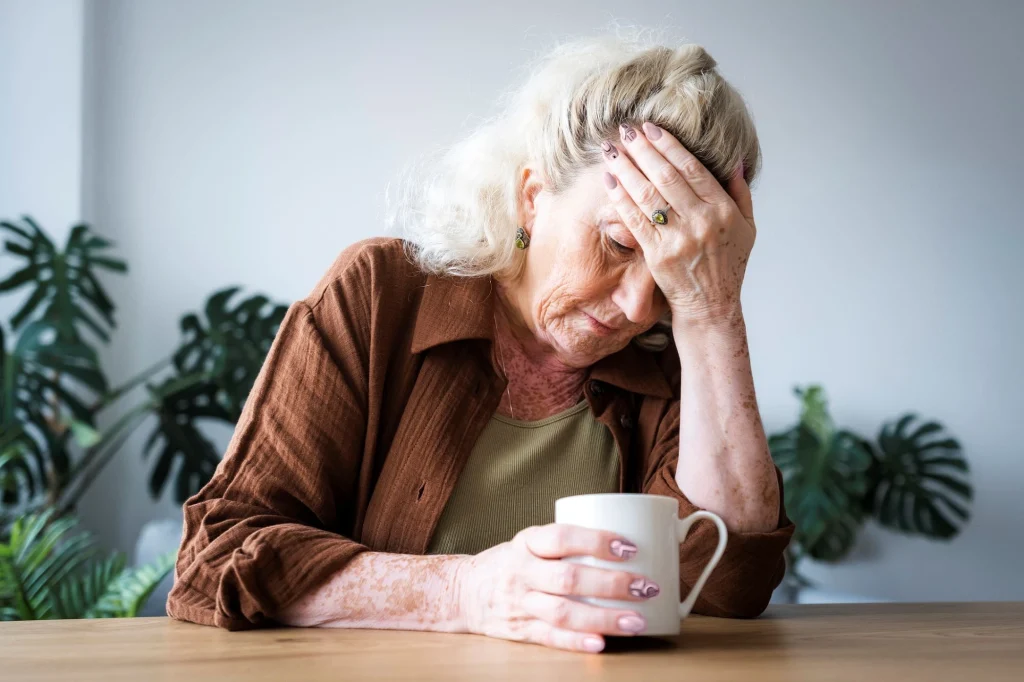 older lady hunched over with migraine clutching cup of coffee