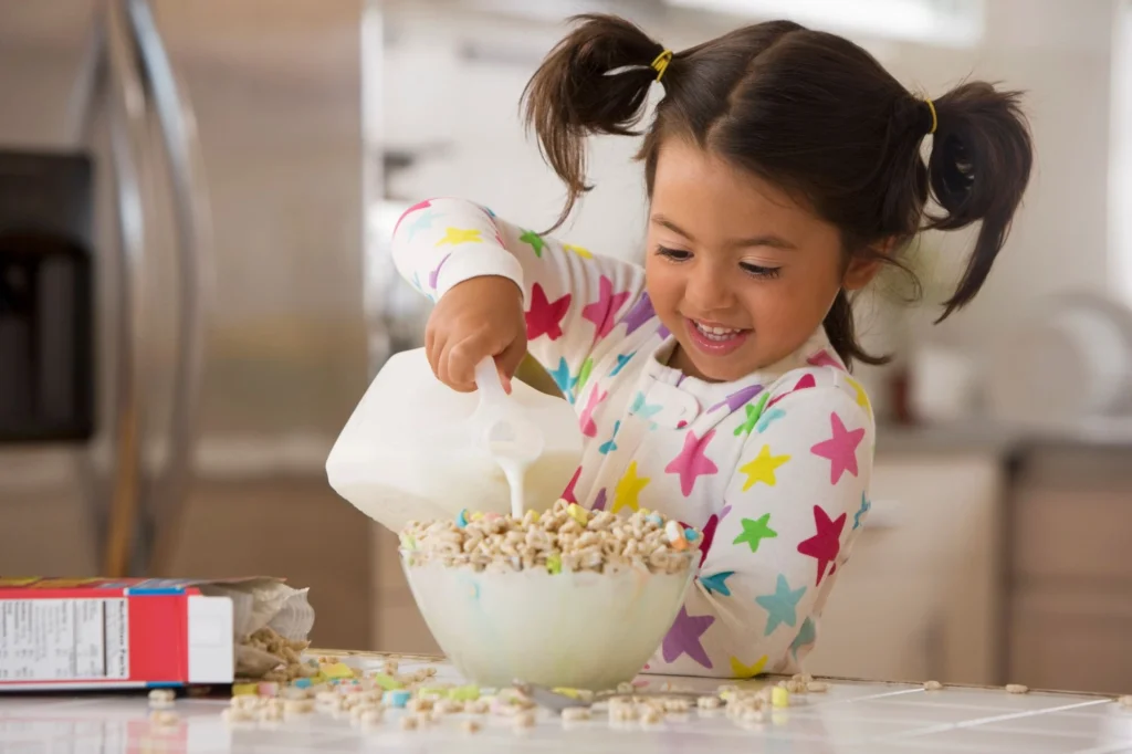 child pouring milk over cereal