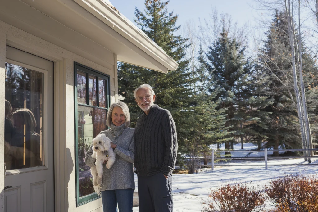 senior couple outside of their home smiling in the snow