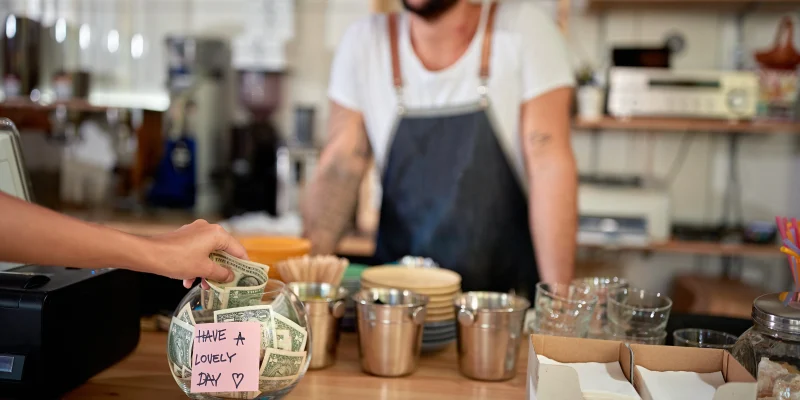 satisfied customer in coffee shop leaving tip in a bowl with a positive message on a sticker. money, tip, satisfied, positive message