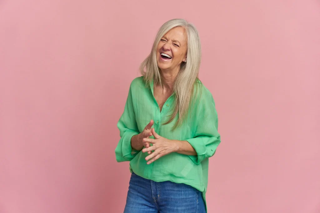 older lady in green shirt laughing pink background