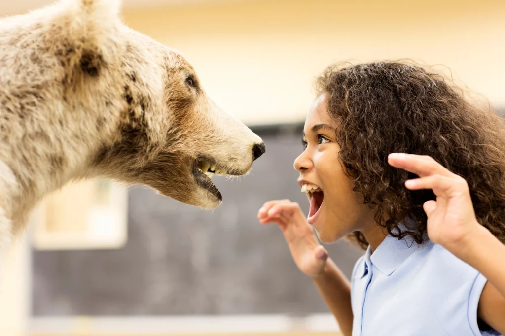 little girl growling at a bear in a museum