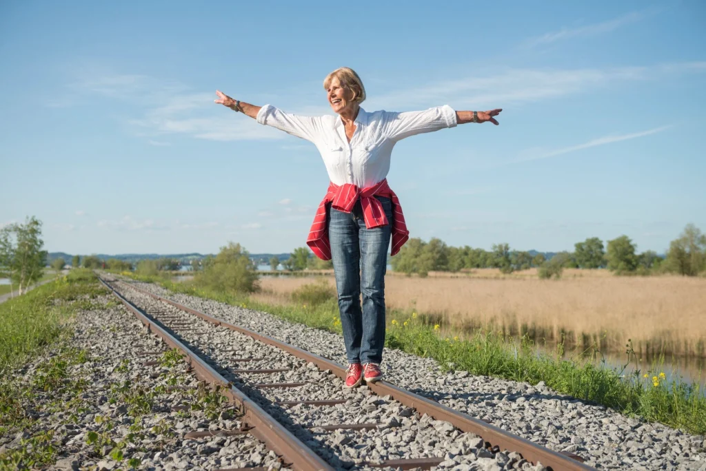 older lady arms splayed to the side balancing on railroad tracks