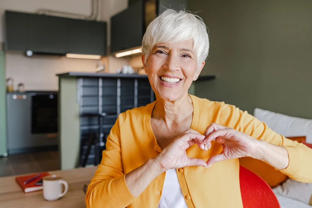 older lady in a yellow sweater heart hands