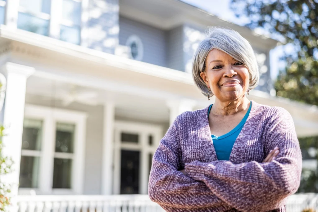 an older lady standing in front of her home smiling