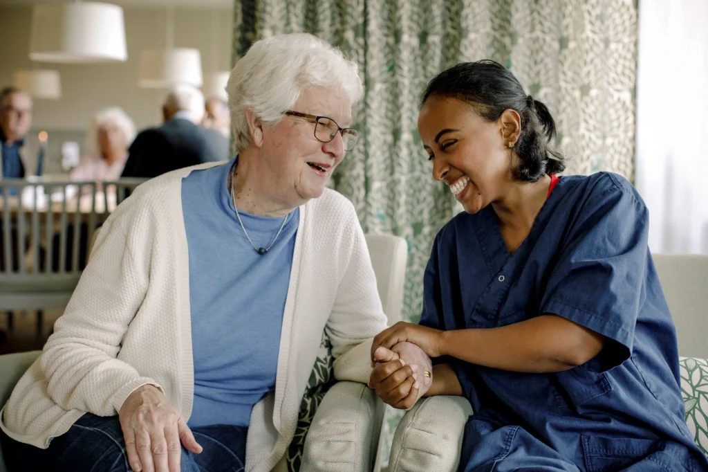 assisted living caregiver and senior woman smiling sitting together