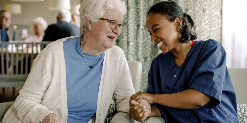 assisted living caregiver and senior woman smiling sitting together