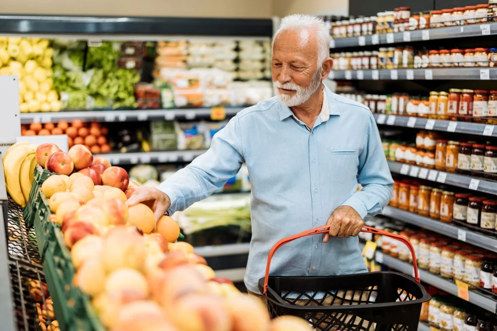 older man gathering fruit grocery shopping in a convenience store