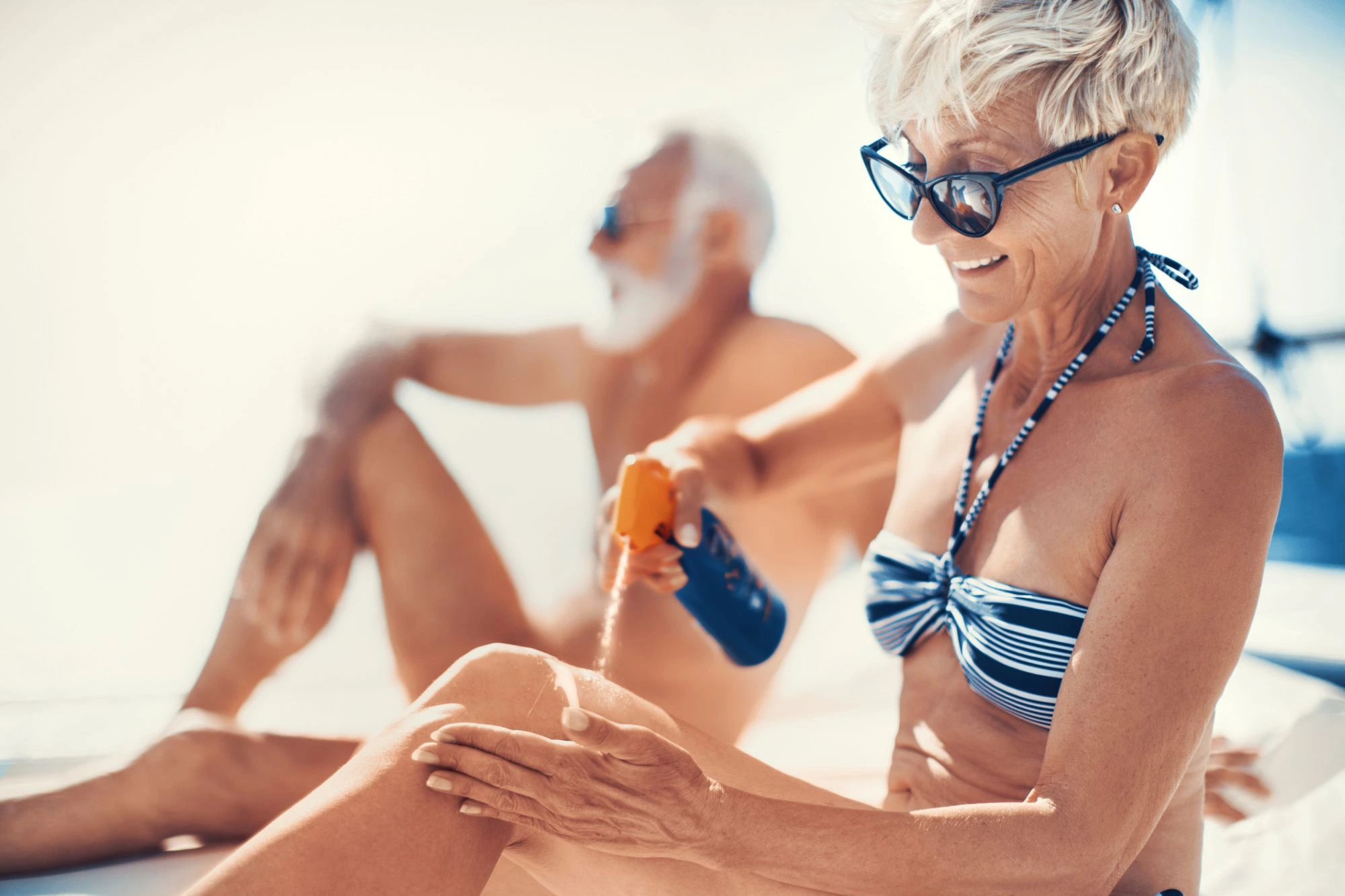 older lady squirting sunscreen on her leg at the beach