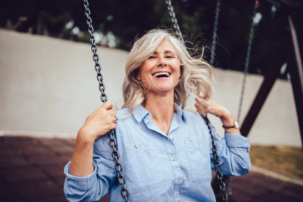older woman with graying blonde hair sitting on a swing and smiling