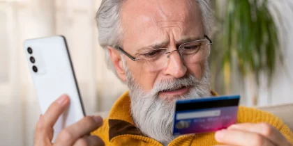 Man holding a phone in one hand and a credit card in the other falling for a scam call.