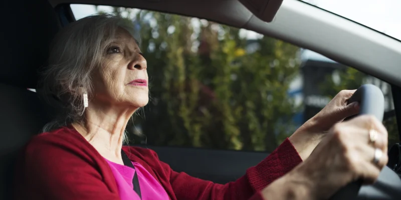 senior woman wearing pink driving a car